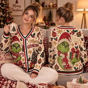 Könnte beinhalten: Eine cremefarbene Strickjacke mit V-Ausschnitt und einem weihnachtlichen Muster aus grünen Grinch-Figuren, roten und grünen Ornamenten, Schneeflocken und Stechpalmen. Auf der Vorderseite steht Merry Grinchmas, auf der Rückseite Custom Name.