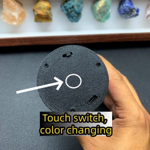 May include: A circular black textured base featuring a touch switch for color changing, a small power toggle, and a USB-C charging port. A white arrow points to the circular touch sensor area, with text reading Touch switch, color changing.
