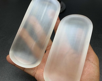 May include: Two elongated, oval-shaped trays carved from translucent, milky white selenite crystal. Each tray features a smooth, polished surface with rounded edges and a shallow, concave center, showcasing the natural fibrous texture of the stone.