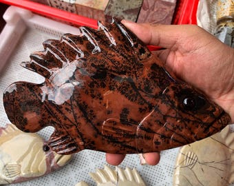 May include: A polished stone carving shaped like a fish, featuring a deep reddish-brown base colour with intricate, dark black dendritic patterns throughout. The fish sculpture has a smooth, glossy finish and a carved eye detail on the side.