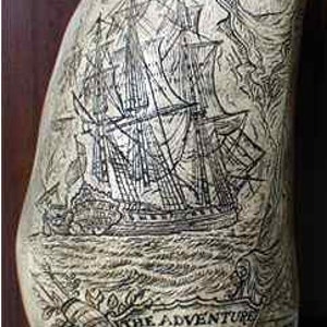 Op de afbeelding: Een gegraveerde walvistand met een gedetailleerde illustratie van een schip, een portret van een man en de tekst "The Adventure Captures the Duepa."