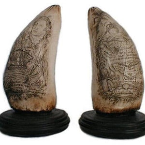 May include: Two antique carved walrus tusks with intricate designs. One tusk features a portrait of a man and a ship, while the other tusk depicts a map with text. Both tusks are mounted on black wooden bases.