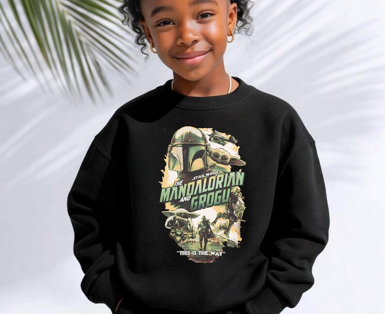 Puede incluir: Una sudadera negra de cuello redondo con un estampado gr&aacute;fico de The Mandalorian y Grogu. El dise&ntilde;o incluye el texto The Mandalorian and Grogu en letras verdes y la frase This is the way en blanco en la parte inferior, con varias ilustraciones.