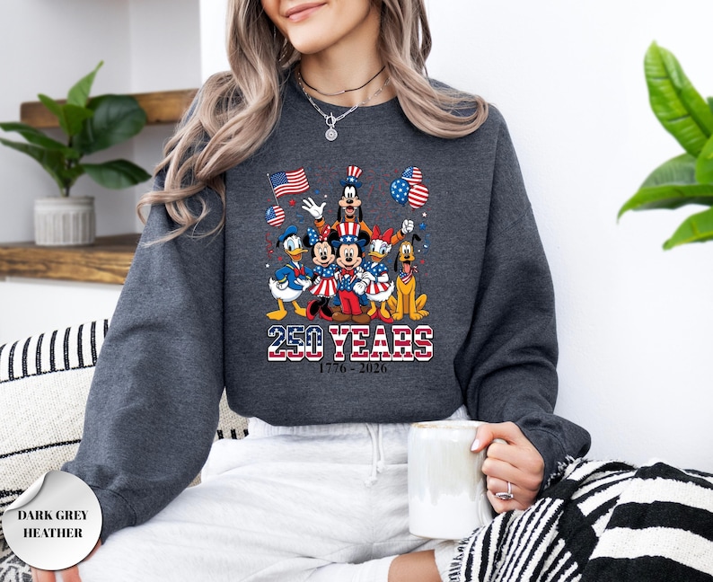 May include: A dark grey heather sweatshirt featuring a graphic of Disney characters including Mickey, Minnie, Donald, Daisy, Goofy, and Pluto wearing patriotic red, white, and blue attire. The text reads 250 YEARS 1776-2026 with American flag motifs.