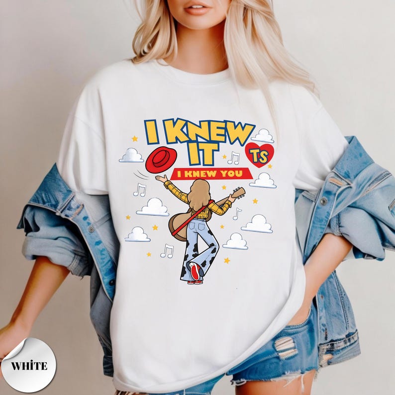 Puede incluir: Una camiseta blanca con el gr&aacute;fico de una persona de pelo largo con camisa de cuadros amarilla y pantalones de campana con estampado de vaca, sosteniendo una guitarra. El texto dice I KNEW IT y I KNEW YOU, rodeado de nubes, estrellas y un coraz&oacute;n.