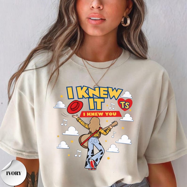 Puede incluir: Una camiseta color marfil con un gr&aacute;fico de una persona de pelo largo tocando la guitarra, con una camisa de cuadros amarilla y pantalones con estampado de vaca. El texto dice I KNEW IT e I KNEW YOU, junto a un sombrero y un coraz&oacute;n rojo.