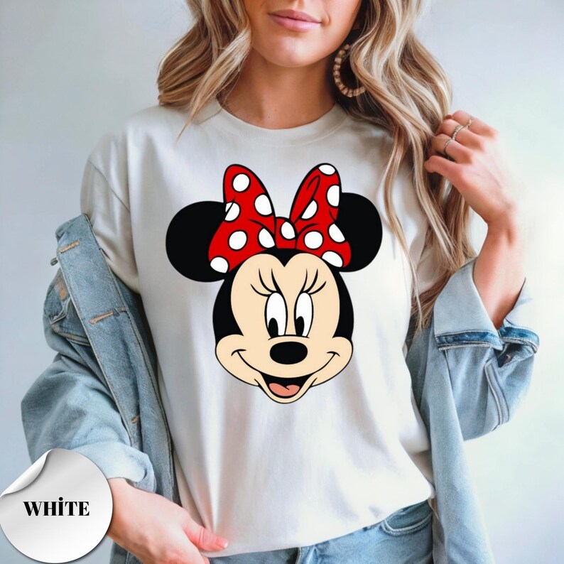 Puede incluir: Camiseta blanca con un gr&aacute;fico de Minnie Mouse. El gr&aacute;fico muestra la cara de Minnie Mouse, con un lazo rojo con lunares blancos. La palabra "WHITE" est&aacute; impresa en una pegatina blanca en la esquina inferior izquierda.