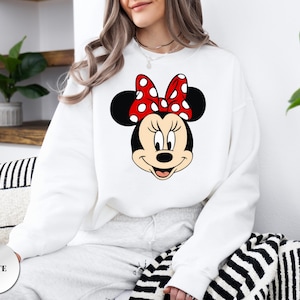 May include: White sweatshirt with a Minnie Mouse design. The graphic depicts Minnie's face, with black ears and a red bow with white polka dots. The word "WHITE" is printed on a white circle in the lower left corner.