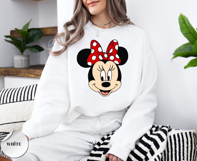 May include: White sweatshirt with a Minnie Mouse design. The graphic depicts Minnie's face, with black ears and a red bow with white polka dots. The word "WHITE" is printed on a white circle in the lower left corner.
