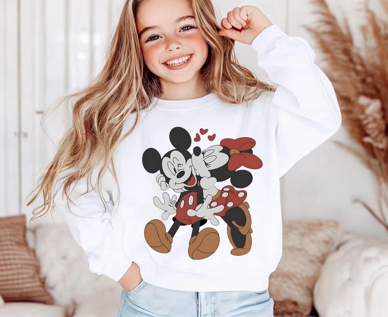 May include: White sweatshirt featuring a graphic of Mickey Mouse and Minnie Mouse kissing, with red hearts. Mickey is wearing red shorts and brown shoes, while Minnie has a red bow and polka dot skirt. The sweatshirt is a casual style.