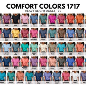 Op de afbeelding: Een display van Comfort Colors 1717 heavyweight volwassen t-shirts in verschillende kleuren. De afbeelding toont een breed scala aan tinten, waaronder Banana, Black, Blossom, Blue Jean en meer. Elke kleur wordt getoond op een t-shirt.
