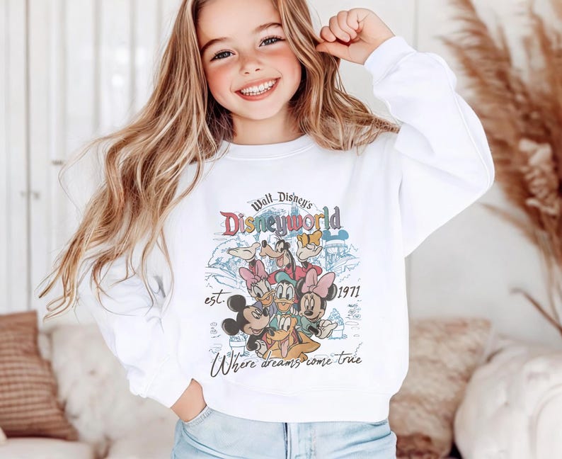 Op de afbeelding: Witte sweatshirt met een kleurrijke afbeelding van Disney-personages, waaronder Mickey Mouse, Minnie Mouse en Donald Duck. Het ontwerp bevat de tekst "Walt Disney's Disneyworld" en "Where dreams come true."