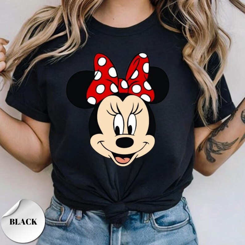 Puede incluir: Camiseta negra con un gr&aacute;fico de Minnie Mouse. El gr&aacute;fico muestra la cara de Minnie, un lazo rojo con lunares blancos. La camiseta tiene cuello redondo y mangas cortas. La palabra "BLACK" est&aacute; impresa en una pegatina blanca.
