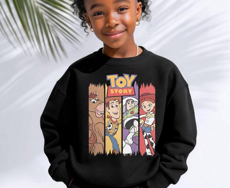 K&ouml;nnte beinhalten: Ein schwarzes Sweatshirt mit Rundhalsausschnitt und einem Grafikdruck der Toy Story-Figuren Bullseye, Woody, Buzz Lightyear und Jessie. Das Design zeigt das Toy Story-Logo in gelber und roter Schrift &uuml;ber den vier vertikalen Charakterfeldern.