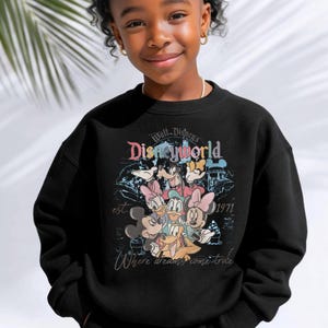 Op de afbeelding: Zwart sweatshirt met een kleurrijke afbeelding van Disney-personages, waaronder Mickey Mouse, Minnie Mouse, Donald Duck en Goofy. Het ontwerp bevat de tekst "Walt Disney World" en "est. 1971". De zin "Where dreams come true" is ook opgenomen.