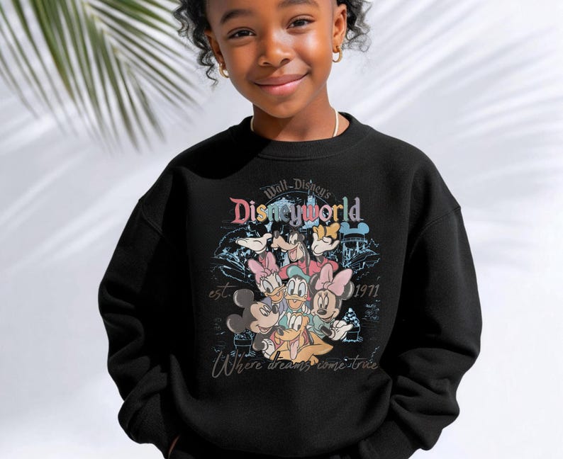 Op de afbeelding: Zwart sweatshirt met een kleurrijke afbeelding van Disney-personages, waaronder Mickey Mouse, Minnie Mouse, Donald Duck en Goofy. Het ontwerp bevat de tekst "Walt Disney World" en "est. 1971". De zin "Where dreams come true" is ook opgenomen.