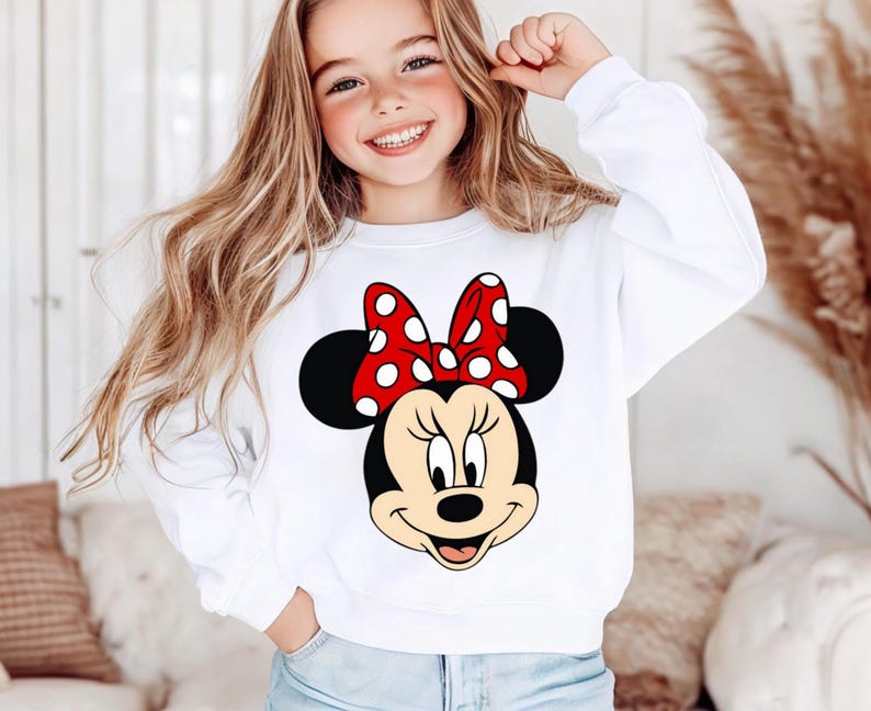 May include: White sweatshirt with a Minnie Mouse graphic. The design shows Minnie's face, including a red bow with white spots, black ears, and a smiling expression. A classic, comfortable style.