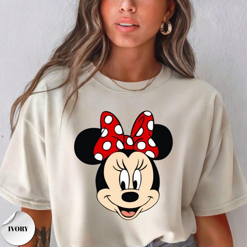 Op de afbeelding: Ivoor kleurig T-shirt met een Minnie Mouse afbeelding. De afbeelding toont Minnie's gezicht met zwarte oren, een rode strik met witte stippen en een lachende uitdrukking. Het T-shirt is een casual stijl.