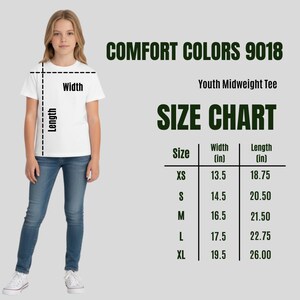 Op de afbeelding: Een persoon draagt een wit T-shirt en een blauwe spijkerbroek. De afbeelding bevat een maattabel voor een jeugd-midweight T-shirt, met afmetingen in inches voor maten XS tot XL. De tekst "COMFORT COLORS 9018" is ook zichtbaar.