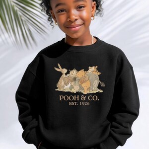 May include: Black sweatshirt featuring a graphic of Winnie the Pooh and friends. The text "POOH & CO. EST. 1926" is printed below the illustration. The sweatshirt is made of a soft material and is suitable for children.