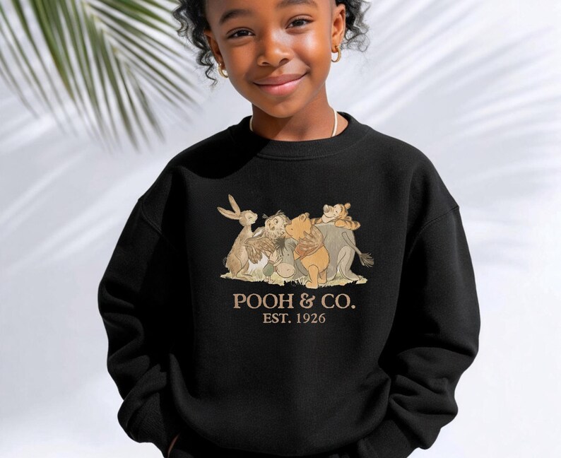 May include: Black sweatshirt featuring a graphic of Winnie the Pooh and friends. The text "POOH & CO. EST. 1926" is printed below the illustration. The sweatshirt is made of a soft material and is suitable for children.