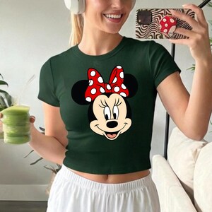 Puede incluir: Top corto verde oscuro con un gr&aacute;fico de Minnie Mouse. El gr&aacute;fico muestra la cara de Minnie con un lazo rojo de lunares. La parte superior tiene mangas cortas y cuello redondo. La camisa est&aacute; hecha de un material suave y c&oacute;modo.
