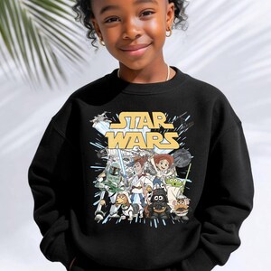 Puede incluir: Una sudadera negra de cuello redondo con un estampado gr&aacute;fico que muestra el logotipo amarillo de Star Wars en la parte superior. Debajo del texto, varios personajes est&aacute;n ilustrados en un estilo combinado, incluyendo figuras de exploradores.