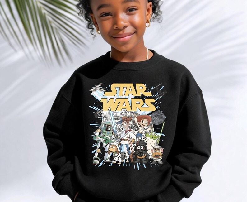Puede incluir: Una sudadera negra de cuello redondo con un estampado gr&aacute;fico que muestra el logotipo amarillo de Star Wars en la parte superior. Debajo del texto, varios personajes est&aacute;n ilustrados en un estilo combinado, incluyendo figuras de exploradores.