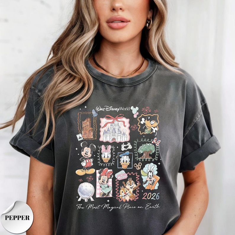 K&ouml;nnte beinhalten: Dunkelgraues T-Shirt mit einer farbenfrohen Grafik von Disney-Figuren und Wahrzeichen. Das Design zeigt Micky Maus, Donald Duck und Aschenputtels Schloss mit dem Text "Walt Disney World" und "2026". Das Shirt ist ein bequemer, l&auml;ssiger Stil.