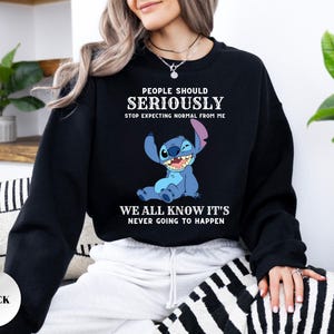 May include: A black crewneck sweatshirt featuring a graphic of the blue character Stitch from Lilo & Stitch. The text reads: PEOPLE SHOULD SERIOUSLY STOP EXPECTING NORMAL FROM ME WE ALL KNOW IT'S NEVER GOING TO HAPPEN in white lettering.