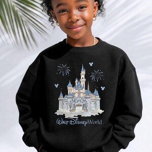 May include: A black long-sleeve sweatshirt featuring a graphic print of a light blue and white castle with fireworks and small Mickey Mouse head silhouettes. The text Walt Disney World is printed in light blue below the castle illustration.