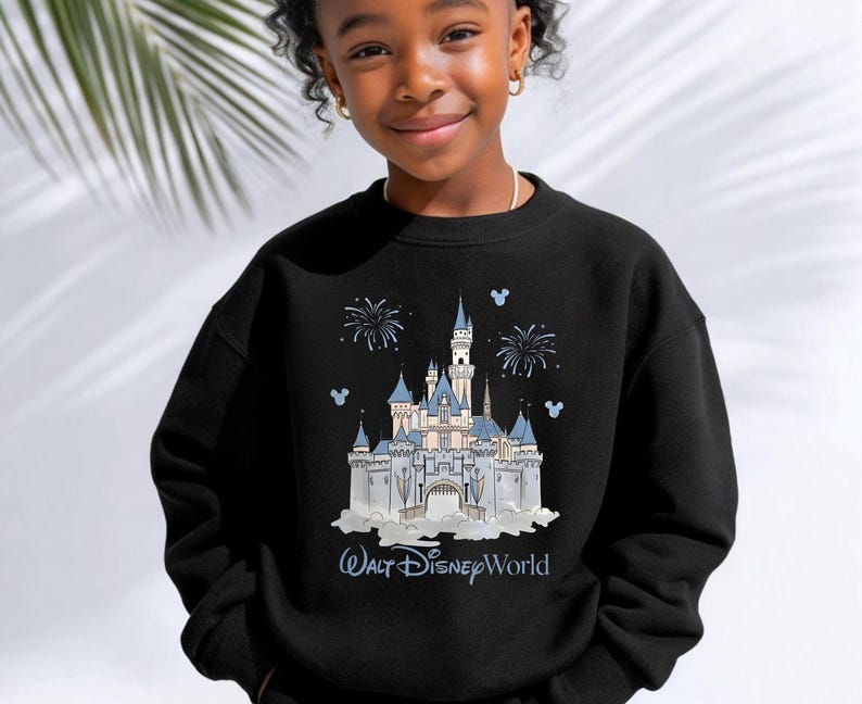 May include: A black long-sleeve sweatshirt featuring a graphic print of a light blue and white castle with fireworks and small Mickey Mouse head silhouettes. The text Walt Disney World is printed in light blue below the castle illustration.