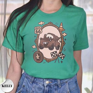 May include: A bright green short-sleeve t-shirt featuring a graphic of a brown tow truck inside an oval frame. The design includes a Route 66 sign, a traffic cone, a tire, and two checkered flags. The shirt has a crew neckline and a casual fit.
