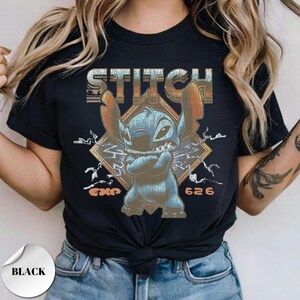 May include: A black short-sleeve t-shirt featuring a graphic of the character Stitch with arms crossed. The design includes the text STITCH in a distressed font, a diamond-shaped background with lightning bolts, and the text EXP 626 in orange.