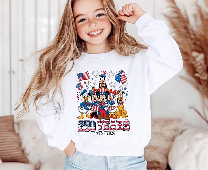 May include: A white long-sleeve sweatshirt featuring a graphic of Disney characters including Mickey Mouse, Minnie Mouse, Donald Duck, Daisy Duck, Goofy, and Pluto dressed in patriotic attire with American flags, balloons, and the text 250 YEARS 1776-2026.