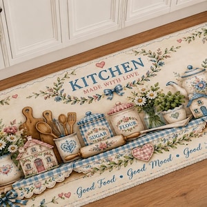 May include: A rectangular kitchen floor mat with a cream background featuring illustrations of houses, flowers, wooden spoons, a rolling pin, and canisters labeled SUGAR and FLOUR. Text reads KITCHEN MADE WITH LOVE and Good Food Good Mood Good Life.