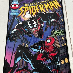 May include: A rectangular plush blanket featuring a comic book cover design of Spider-Man and Venom. The blanket has a black border and displays the text "The Sensational Spider-Man" and "To Catch a Spider". The background is a cityscape.
