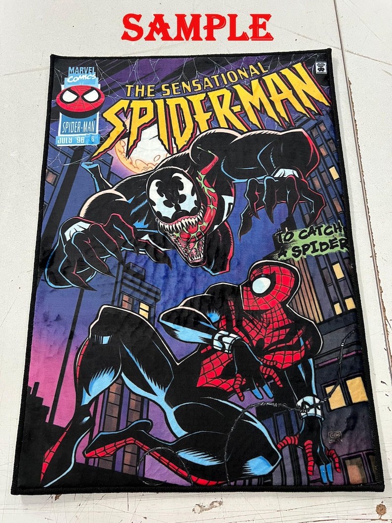 May include: A rectangular plush blanket featuring a comic book cover design of Spider-Man and Venom. The blanket has a black border and displays the text "The Sensational Spider-Man" and "To Catch a Spider". The background is a cityscape.