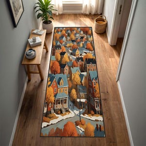 Puede incluir: Una alfombra rectangular para pasillo con una colorida ilustración de un pueblo con casas y árboles en colores otoñales. La alfombra tiene un borde negro y está colocada sobre un suelo de madera.