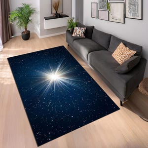 May include: A rectangular area rug with a celestial design. The rug features a dark blue background with a bright white starburst pattern in the center, surrounded by small white stars. The rug is placed on a light-colored wooden floor.