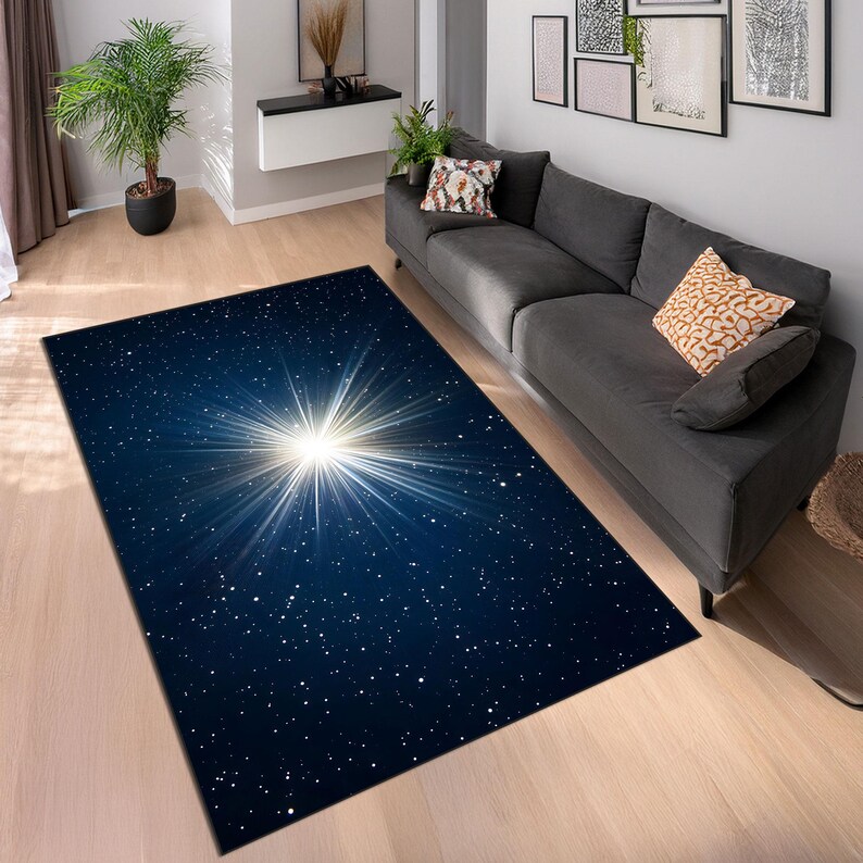 May include: A rectangular area rug with a celestial design. The rug features a dark blue background with a bright white starburst pattern in the center, surrounded by small white stars. The rug is placed on a light-colored wooden floor.