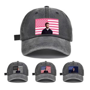 Op de afbeelding: Een grijze baseballcap met een roze Amerikaanse vlag en een persoon ervoor. De cap heeft een gebogen klep en een verstelbare band. Extra caps met vergelijkbare ontwerpen worden hieronder getoond.