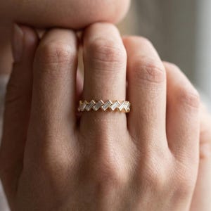 May include: A gold ring with a repeating pattern of baguette-cut diamonds. The ring is set in a yellow gold band and is worn on a finger. The diamonds are clear and sparkling.