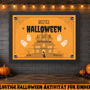 May include: A framed Halloween-themed sign with the words "BESTES HALLOWEEN KOST&Uuml;M" in black on an orange background. The sign features a haunted house graphic, ghosts, and spiderwebs. Pumpkins and candles are in the foreground.