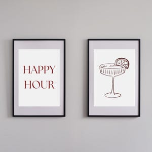 Könnte beinhalten: Zwei gerahmte Drucke mit schwarzen Rahmen. Der linke Druck zeigt die Worte "HAPPY HOUR" in Burgunderrot. Der rechte Druck zeigt eine Strichzeichnung eines Cocktailglases mit einer Zitronenscheibe.