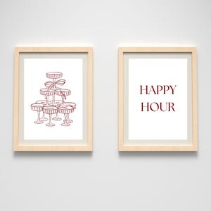 Könnte beinhalten: Zwei gerahmte Drucke mit hellen Holzrahmen. Ein Druck zeigt eine Strichzeichnung eines Champagnerglasturms, der mit einer Schleife gebunden ist. Der andere Druck hat die Worte "HAPPY HOUR" in einer burgunderroten Schrift.