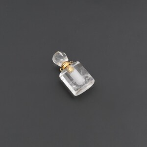 May include: A small, clear, rectangular perfume bottle pendant crafted from faceted crystal. It features a gold-toned metal neck and a matching crystal stopper, with two small gold loops attached to the neck for hanging as a piece of jewelry.