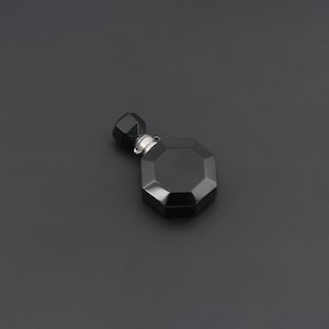May include: A small, black, octagonal-shaped perfume bottle with a faceted surface. The bottle features a matching black, faceted, geometric stopper and a silver-toned metal collar connecting the stopper to the main body of the container.