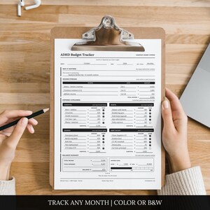 May include: A printed ADHD Budget Tracker document secured on a brown clipboard. The form features sections for income streams, expense categories, savings, debt payoff, and a balance summary with black text on a white background for monthly tracking.