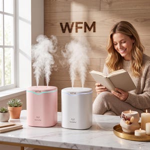 May include: Two H2O Humidifier units, one in pastel pink and one in white, each emitting a steady stream of mist. Both devices feature the WFM logo on the front, a sleek cylindrical shape, and a thin glowing light strip near the top edge.